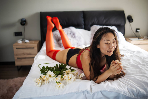 Sexy young girl laying in white bed with flowers - branch of fresh roses on 8 March - Foto, immagini