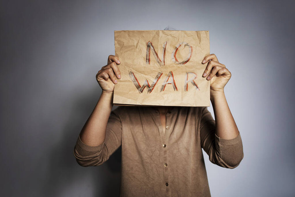 arkusz papieru rzemieślniczego z czerwonym napisem kolor nie wojny. Zdenerwowana biedna dziewczyna protestująca przeciwko wojnie podnosi sztandar z napisem "No War". Kryzys, pokój, powstrzymanie agresji. - Zdjęcie, obraz