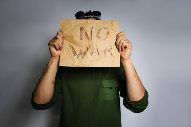sheet of craft paper with white color inscription no war. Upset male protesting war conflict raises banner with inscription message text No War. Crisis, peace, stop aggression. - Photo, Image