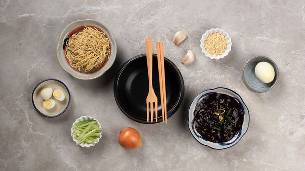 空のつくばえぎ平置きのコンセプト黒豆のソースをかけた韓国麺「チャンミョン」または「チャンミョン」の材料。灰色のセメントの木の背景に  - 写真・画像