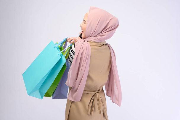 A young beautiful muslim woman in suit holding colorful shopping bags over white background studio - Фото, зображення
