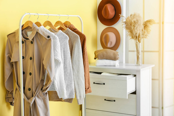 Σχάρα με ζεστά ρούχα κοντά σε κίτρινο τοίχο στην αίθουσα - Φωτογραφία, εικόνα
