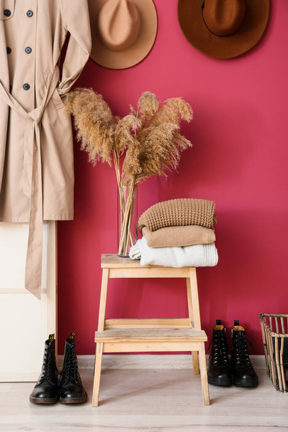 Taburete de paso con suéteres calientes y jarrón cerca de la pared rosa en el pasillo - Foto, Imagen