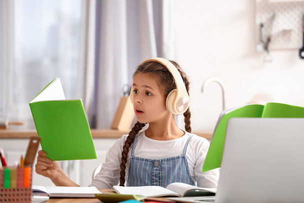 Shocked little girl in headphones with copybooks studying online at home - Photo, Image