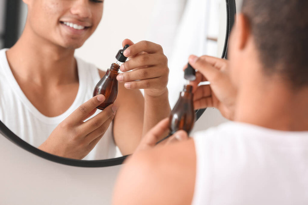 Молодий афроамериканець використовує сироватку для догляду за шкірою у ванній кімнаті. - Фото, зображення