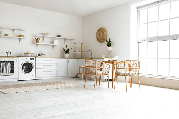 Інтер'єр світлої кухні з пральною машиною, білими лічильниками та обіднім столом
 - Фото, зображення