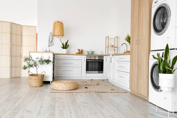 Интерьер светлой кухни со стиральной машиной, белыми столешницами и шкафом - Фото, изображение