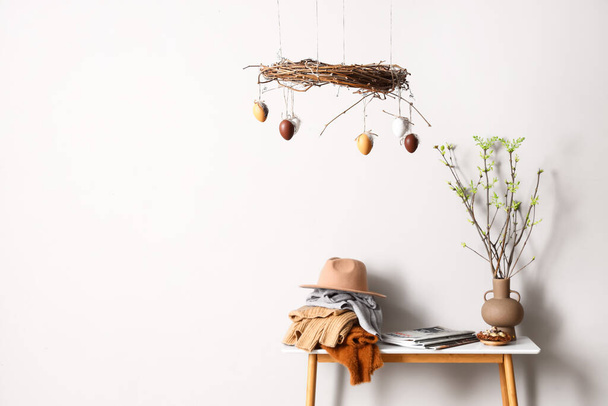 Different clothes, tree branches on table and stylish Easter decor near light wall - Photo, Image
