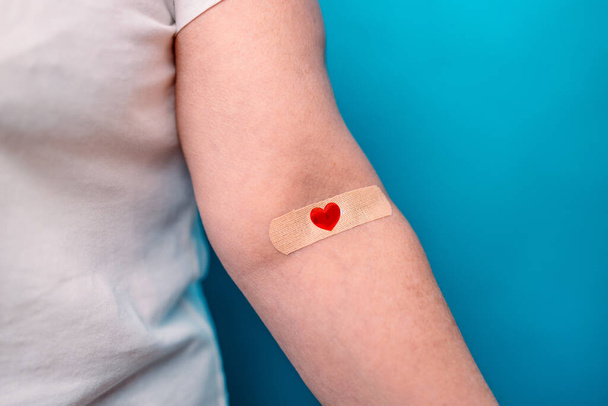 Blood donation donorship. Blood donor with bandage after giving blood on blue background. Healthcare and world cancer day concept - Foto, afbeelding