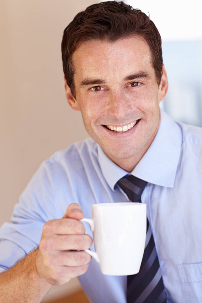 Enjoying his morning coffee. Smiling young businessman enjoying his coffee break. - Foto, Imagen