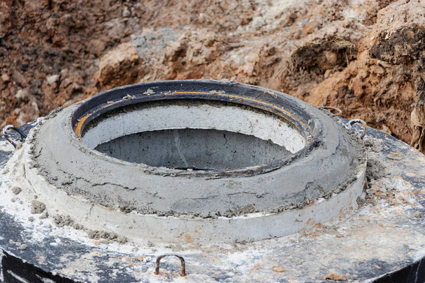 Монтаж железобетонной скважины для водоснабжения и канализации на строительной площадке. Кольца с чугунным люком и строительным инструментом - Фото, изображение