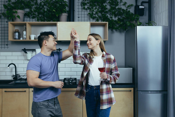 Мужчина и женщина танцуют вместе, веселятся дома, на кухне, в многорасовой семье - Фото, изображение