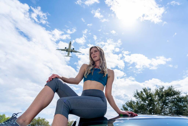 Una bella modella bionda gode di una giornata estiva mentre un aereo commerciale vola sopra la testa - Foto, immagini