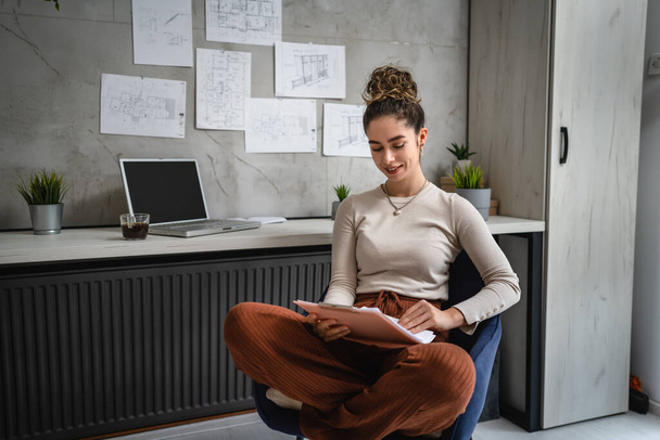 one woman young caucasian female sitting by the desk at work in the office study documents relaxing while hold clip chart with papers real people copy space female engineer or student planning project - Photo, image