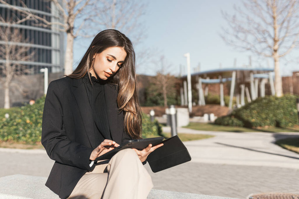 Portrait of successful young caucasian business woman working on tablet sitting outside office area. - Photo, Image