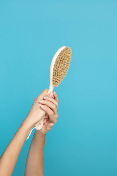 Wooden brush made for massage of dry skin in hands on blue background. Self-care and body-care. Anti-cellulite procedures aiming for getting rid of cellulite - Foto, Imagen