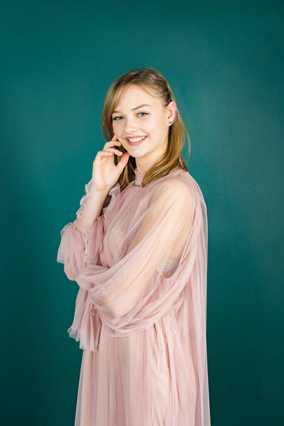 Lachend jong mooi meisje in een roze jurk op een groene achtergrond. Groene achtergrond met kopieerruimte. Kijk in de camera.. - Foto, afbeelding