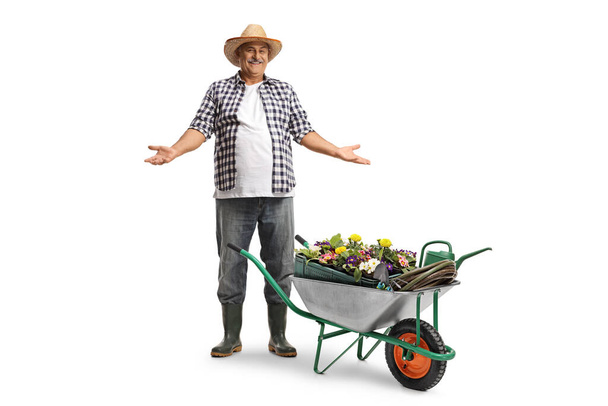 Full length portrait of a smiling mature farmer with a straw hat with a hand cart full of plants isolated on white background - Foto, Bild
