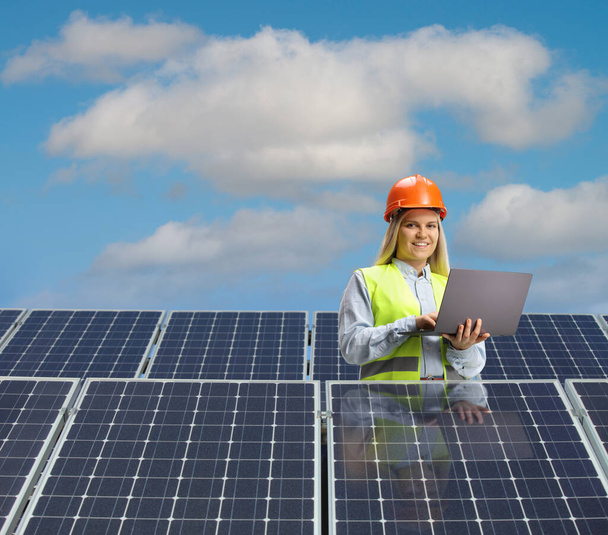 Young female engineer working on a laptop computer behind solar panels  - Foto, Imagem