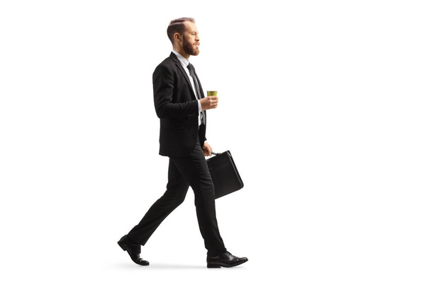 Full length profile shot of a businessman walking with a takeaway coffee cup and a briefcase isolated on white background - Foto, immagini