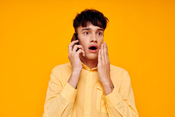 handsome man in a yellow shirt talking on the phone close-up - Fotó, kép
