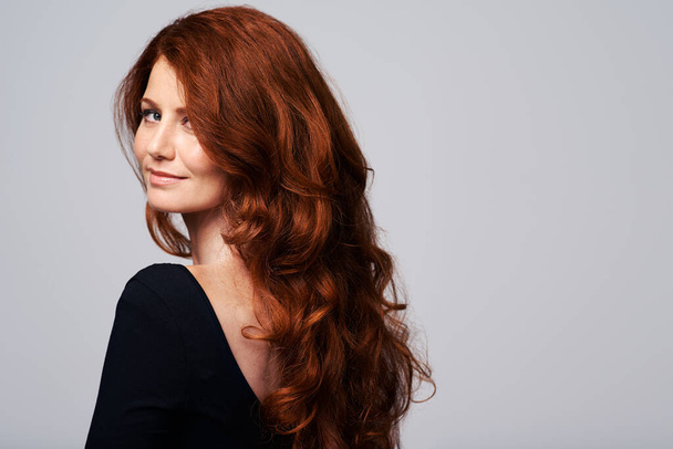Καταπληκτικά μαλλιά. Στούντιο πλάνο μιας νεαρής γυναίκας με όμορφα κόκκινα μαλλιά ποζάρουν σε γκρι φόντο. - Φωτογραφία, εικόνα