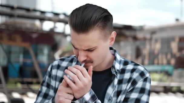 Jonge knappe man met snor in geruit zwart-wit shirt die buiten een sigaret rookt. slechte gewoonte - Video
