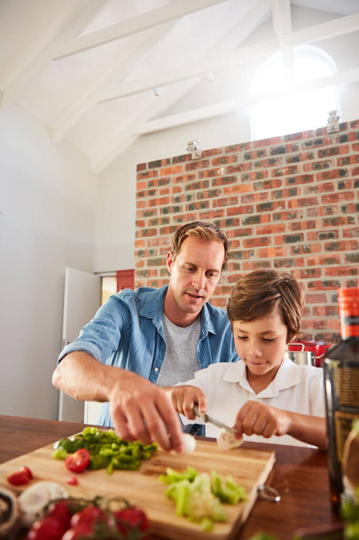 指に気をつけろ相棒。台所で彼の小さな男の子が野菜を切るのを見て父親のショット. - 写真・画像