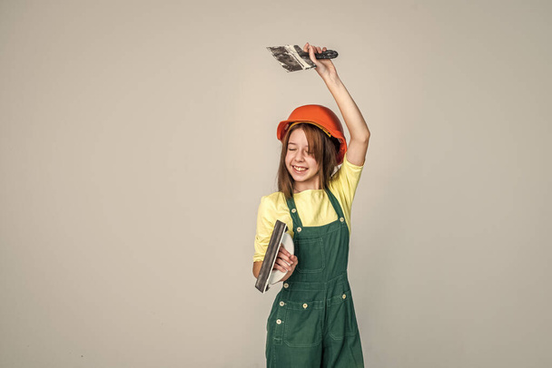 she love job. using working tool. teen girl in helmet and boilersuit with spatula. child wear hard hat. kid builder on construction site. worker engineer. architect in workshop. renovation and repair - Fotografie, Obrázek