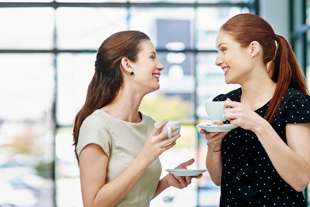 Tell me all about your weekend. Cropped shot of two businesswomen standing and chatting during a coffee break. - Foto, immagini