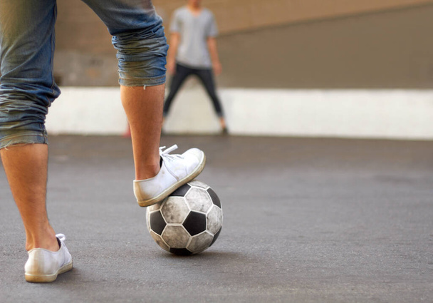 Ready to score. Cropped image of a mans foot on a soccer ball in the street. - Photo, image