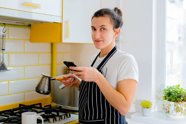 台所でスマートフォンやコーヒーを飲んでいる女性です。コンセプト幸せな朝のレジャー - 写真・画像