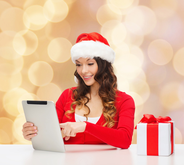 smiling woman in santa hat with gift and tablet pc - Foto, Bild