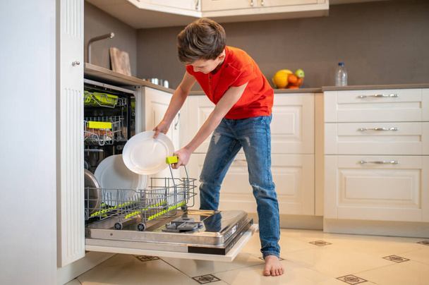 Boy putting dishes into an open dish-washing machine - Fotó, kép