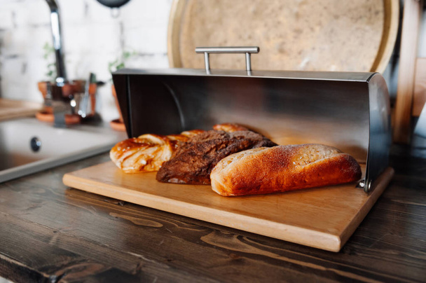 bochníky chleba leží v kovové stříbrné krabici od chleba v dřevěné kuchyni. domácí dorty. selektivní zaměření - Fotografie, Obrázek