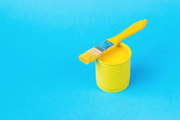 A yellow brush on a jar with yellow paint on a large blue background. Trending colors. Minimal concept of interior selection. - Foto, immagini