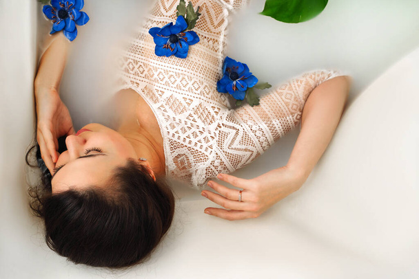 vista superior de la mujer joven y sensual disfrutando del baño de leche con flores azules - Foto, Imagen