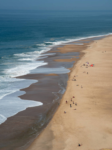 Toeristische mensen ontspannen en zonnebaden op een zandstrand. Nazare Portugal - Foto, afbeelding