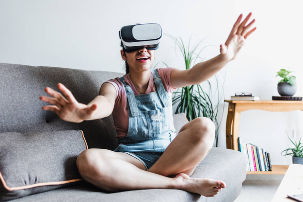 Joven mujer hispana jugando y usando gafas de realidad virtual VR en casa en México América Latina - Foto, Imagen