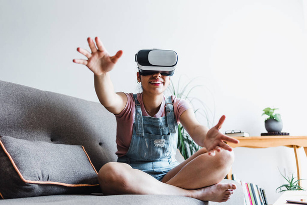 jonge Spaanse vrouw spelen en het gebruik van virtual reality bril VR thuis in Mexico Latijns-Amerika - Foto, afbeelding