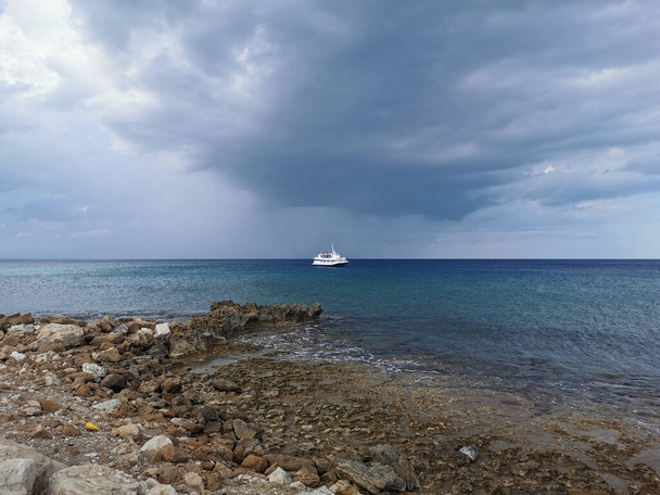 Protaras. Famagustan alue. Kypros. Välimeren kivinen rannikko meren taustalla kävelevä valkoinen laiva ja dramaattinen taivas. - Valokuva, kuva