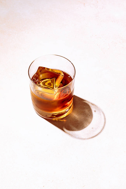 Whiskey or bourbon in a rocks glass with a big ice cube, shot with hard light and harsh shadows, bright backdrop, copy space - Valokuva, kuva