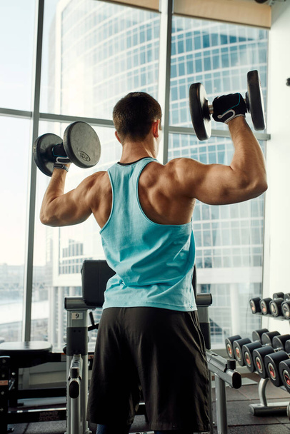 Athletic man shakes his biceps with dumbbell in his hands. Healthy lifestyle concept - Photo, Image
