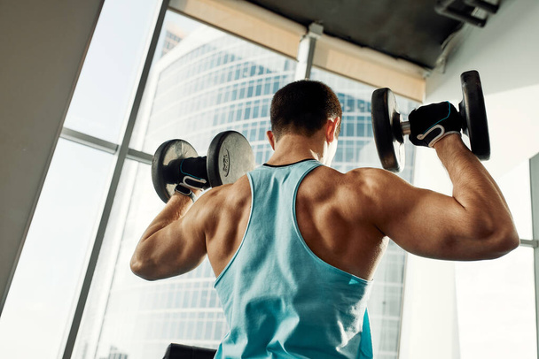 Athletic man shakes his biceps with dumbbell in his hands. Healthy lifestyle concept - Foto, afbeelding