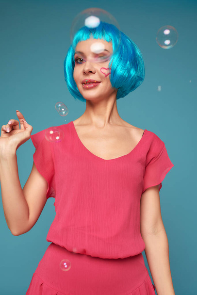 Piękna młoda kobieta z niebieską peruką i jasnym makijażem w bańce mydlane. Modelka dziewczyna model z twórczym makijażem kolor. Koncepcja lalek kobiet. - Zdjęcie, obraz