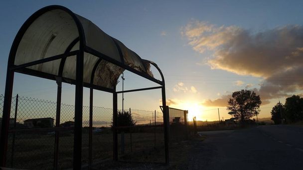 Półzniszczony przystanek autobusowy na przedmieściach o zachodzie słońca. - Zdjęcie, obraz