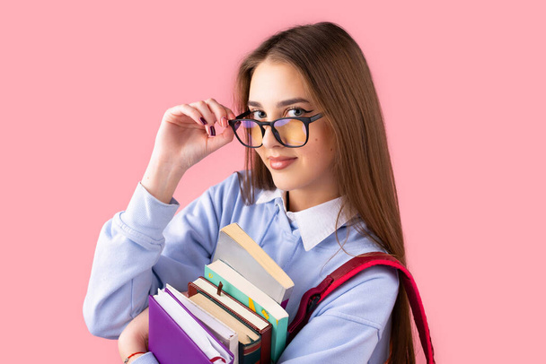 Pretty girl teen student with backpack holds books touching glasses with fingers having smart facial expression, education in high school concept. - Φωτογραφία, εικόνα