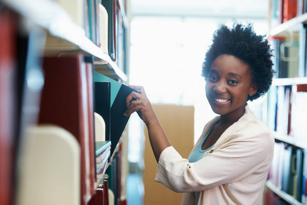 Studeren voor mijn eindexamen. Een jonge vrouw die boeken selecteert in de bibliotheek. - Foto, afbeelding