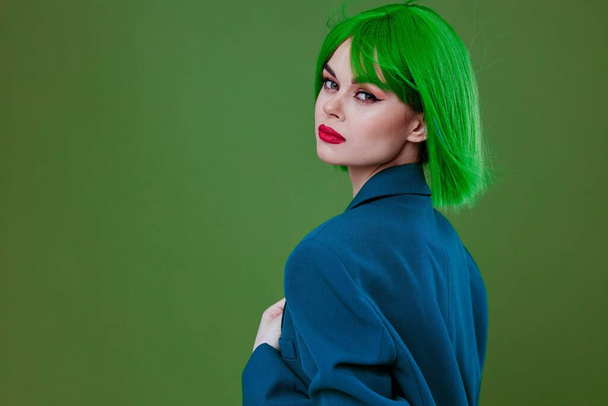 Belleza Mujer de moda con una peluca verde chaqueta azul posando fondo verde inalterado - Foto, imagen