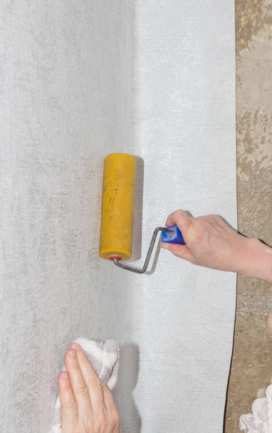 Hand of a woman smoothes air and glue bubbles on the wallpaper with a roller. - Photo, Image